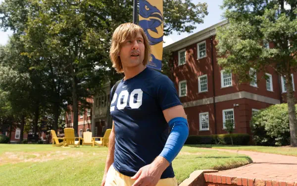 2K Quad HD PC wallpaper featuring TV show character Chad Powers in athletic gear on a sunny college lawn, mid-action with brick dorm and flag visible in the background.