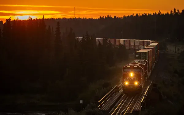 5K Ultra HD desktop wallpaper: freight train on a railroad bridge at sunset, winding through a forested natural landscape.