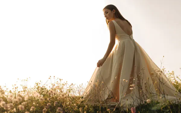 4K Ultra HD PC Desktop Wallpaper and Background — backlit woman in a flowing gown walks through a sunlit wildflower meadow at golden hour.