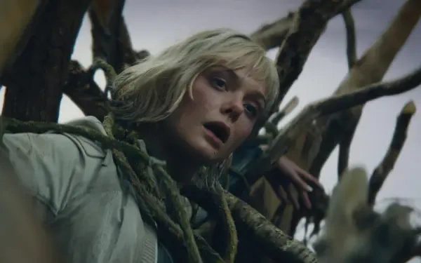 HD PC desktop wallpaper: the lead actress from the movie Predator: Badlands — pale-haired woman tangled in gnarled roots, gazing upward amid moody, dramatic lighting.