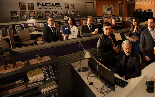 NCIS team in a busy office bullpen with desks, monitors and an evidence board — 2K Quad HD PC desktop wallpaper/background.