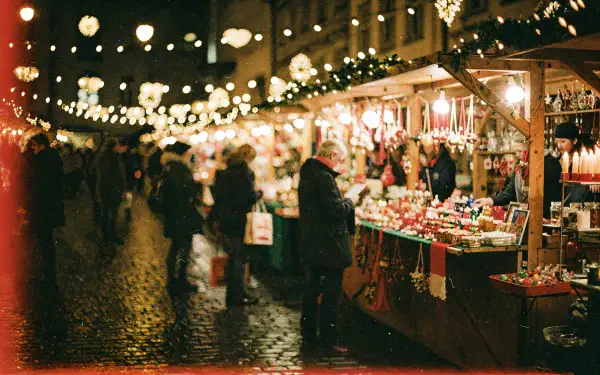 Nighttime Christmas market with twinkling string lights, wooden stalls and blurred shoppers in warm bokeh — 4K Ultra HD PC desktop wallpaper and background.