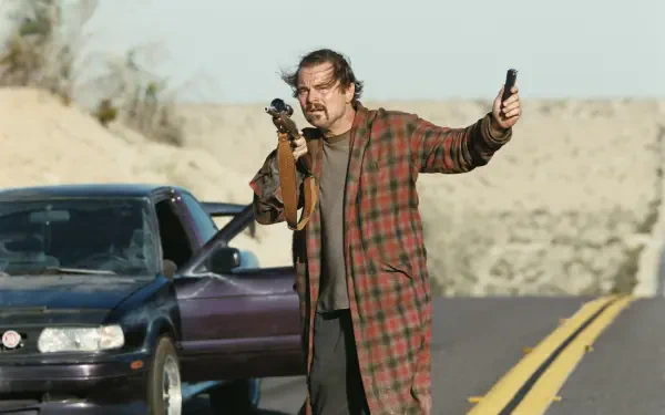 4K Ultra HD PC desktop wallpaper for the movie One Battle After Another: rugged male actor in a plaid coat aiming a rifle, holding a phone beside a car on a desert road.