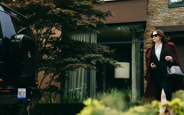 4K Ultra HD PC wallpaper for the movie Bugonia: an actress in sunglasses and a long coat strides away from a modern house, carrying a handbag.