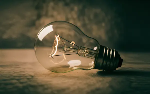 Vintage incandescent light bulb with warm glowing filament on a textured surface, 4K Ultra HD PC desktop wallpaper and background.