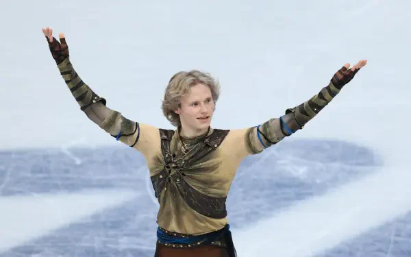 Ice skater at the Winter Olympics, arms raised in a gold-and-green costume on the icy rink — HD PC desktop wallpaper and background.