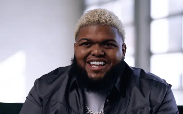 HD PC desktop wallpaper of a smiling male streamer with short bleached-blond hair and a beard, wearing a dark jacket against a soft-lit background.
