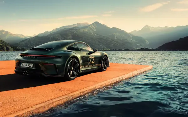 Green Porsche 911 GT3 parked on an orange lakeside pier with soaring mountains at sunrise — 4K Ultra HD PC desktop wallpaper/background.