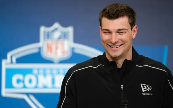 Smiling American man in front of an NFL logo press backdrop, 4K Ultra HD PC desktop wallpaper/background.