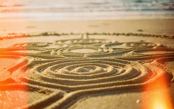 Close-up of intricate circular sand art etched in wet beach sand at sunrise, warm light leaks — 4K Ultra HD PC desktop wallpaper and background.