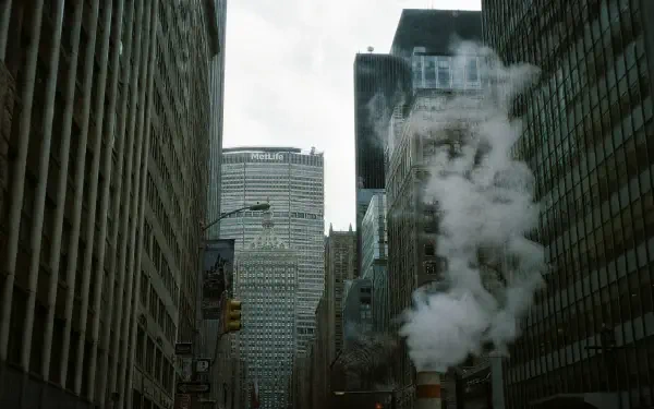 Concrete jungle of towering skyscrapers framing a misty avenue with steam rising from a street vent — 4K Ultra HD PC Desktop Wallpaper and Background.