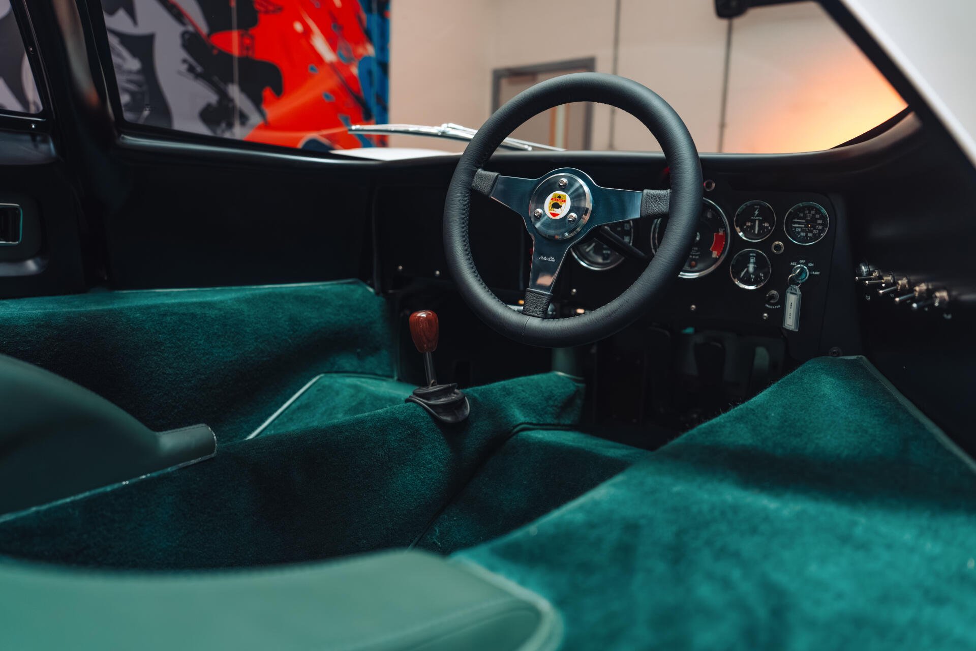 Vehicle interior of a McLaren G6GT: teal suede cockpit, classic steering wheel and manual shifter — 8K Ultra HD PC desktop wallpaper/background.