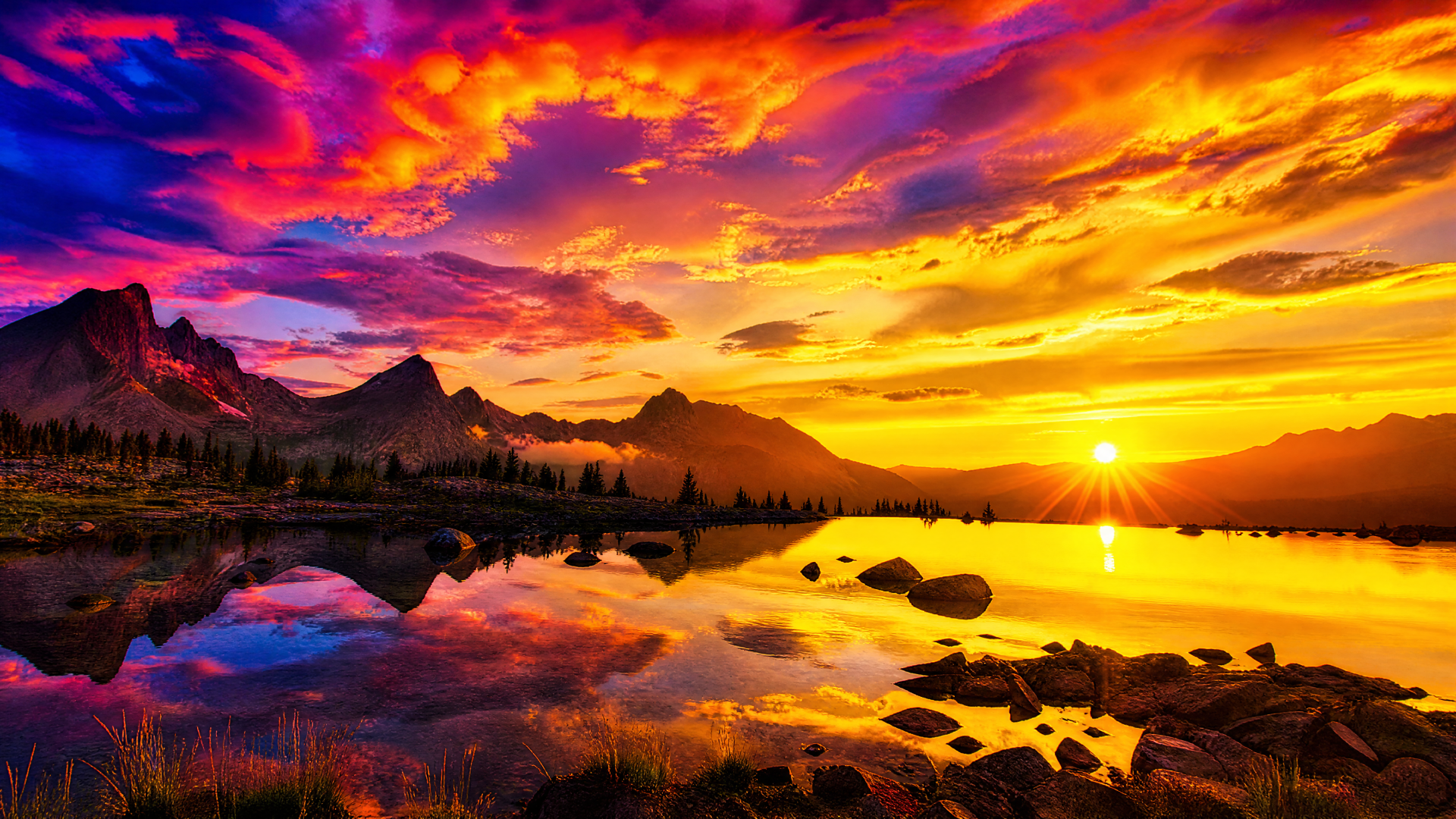 4K Ultra HD PC desktop wallpaper and background: golden sunrise over jagged mountains reflected in a glassy lake, vivid multicolored sky and rocky shoreline landscape.