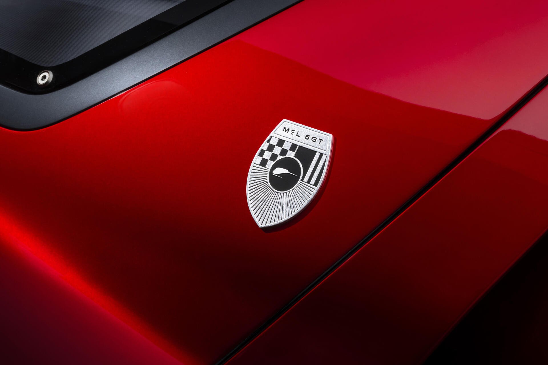 Close-up of a red McLaren McL 6GT hood and badge with high-gloss finish; 5K Ultra HD PC desktop wallpaper background.