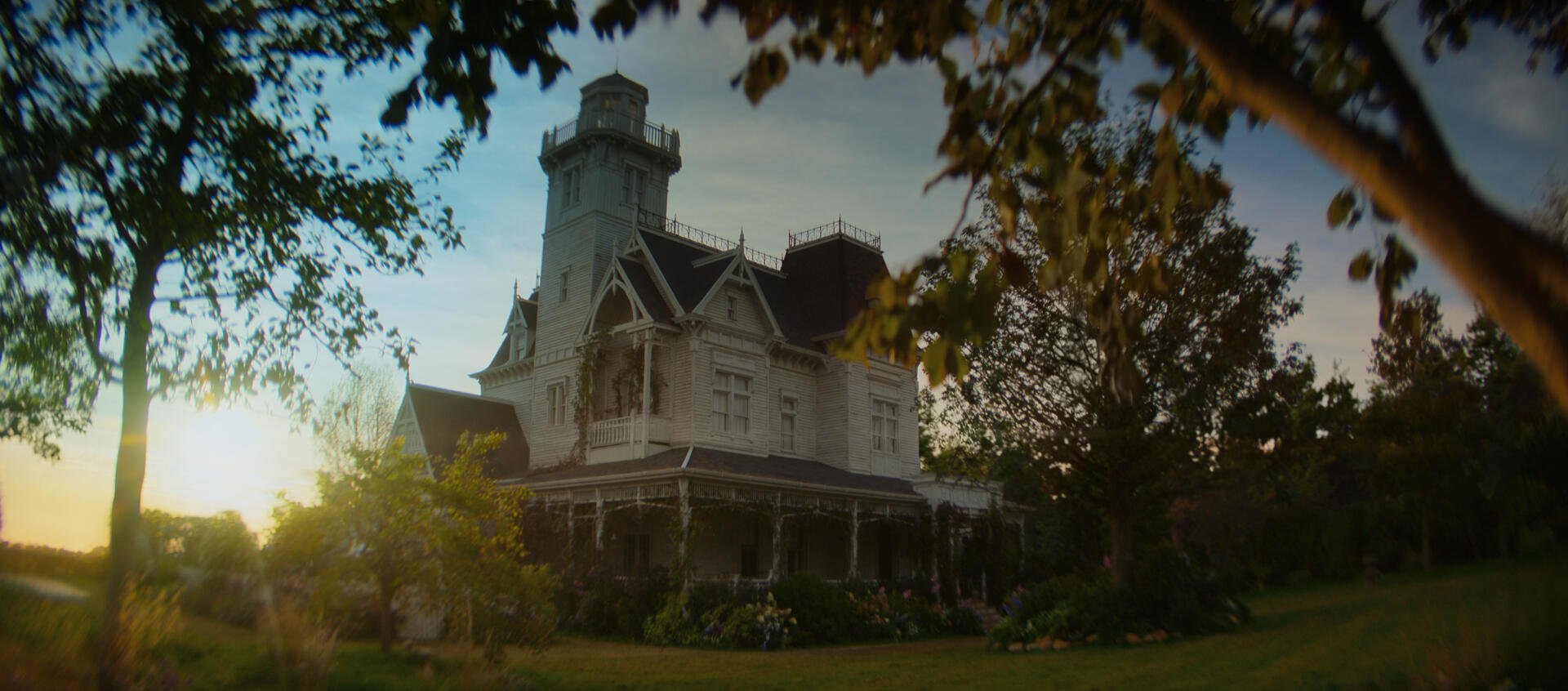 Victorian Owens House mansion from Practical Magic 2 at sunset, framed by trees — 2K Quad HD PC desktop wallpaper background.