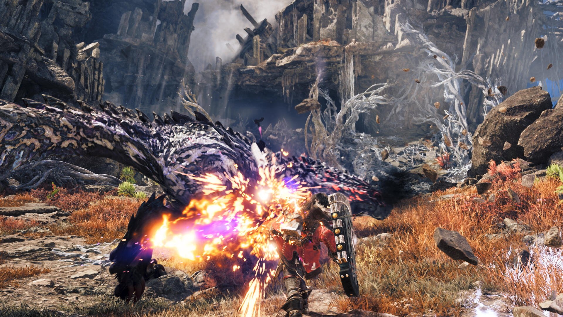 Monster Hunter Wilds — Ascendance: a hunter clashes with a colossal dragon monster amid rocky wilds, a fiery blast illuminating the fight. 4K Ultra HD PC desktop wallpaper and background.
