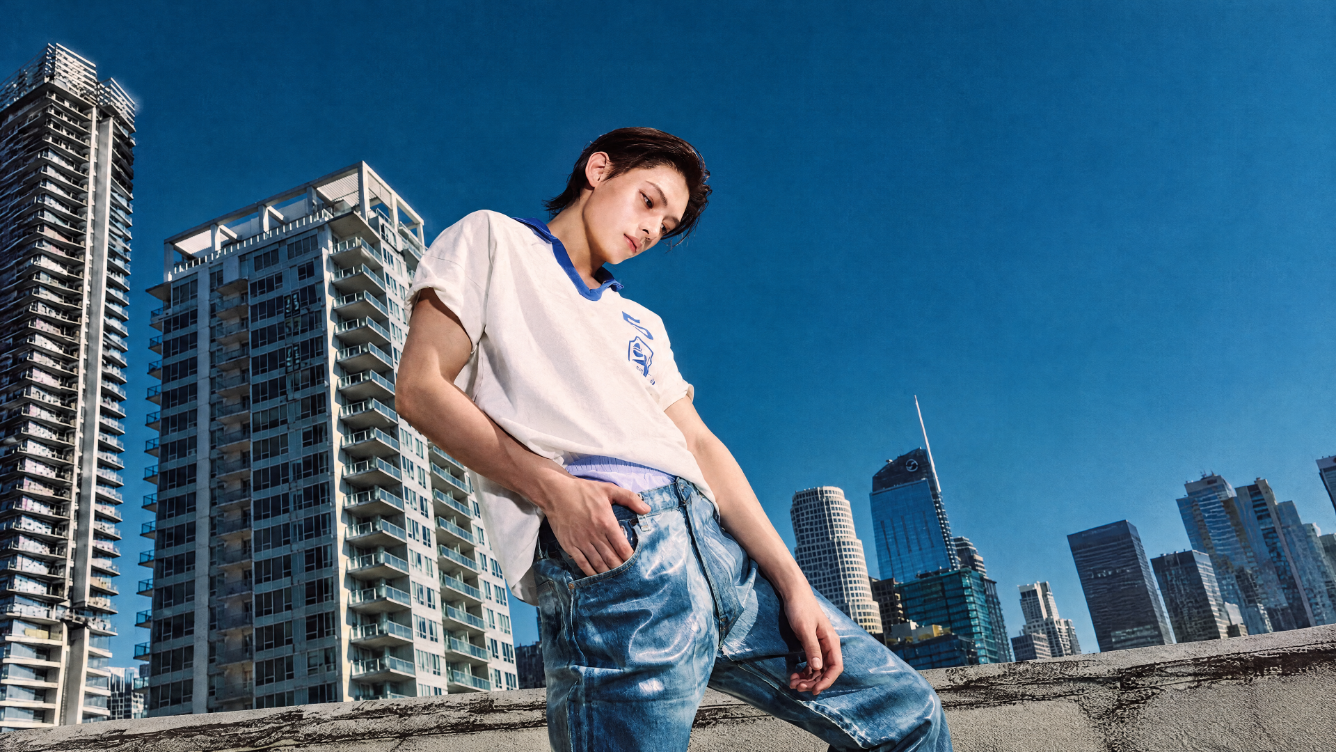 Cortis — Color Outside the Lines 4K Ultra HD PC wallpaper: young man on a rooftop, leaning against a railing with a skyscraper cityscape under a clear blue sky.
