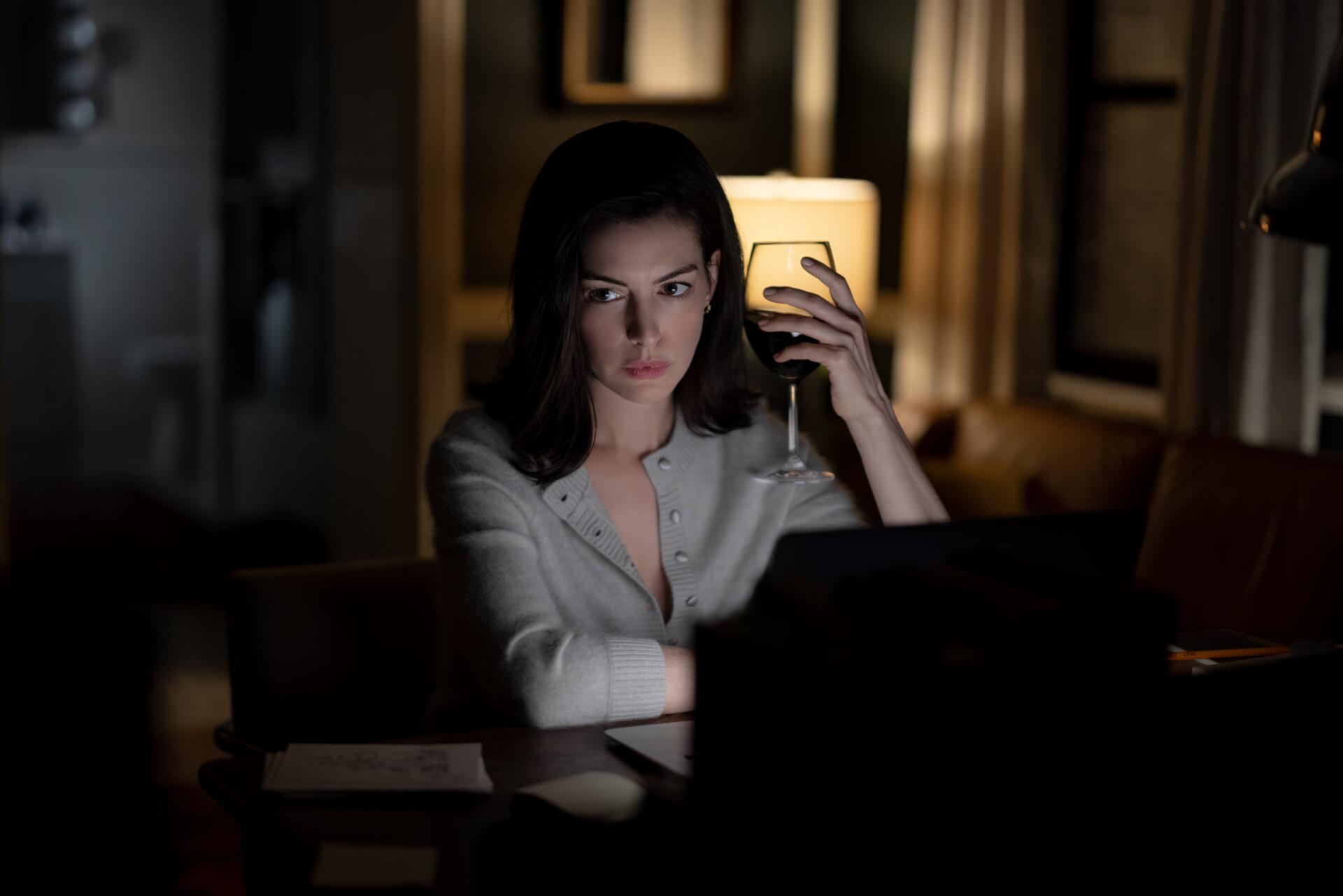 Anne Hathaway as Verity in a dimly lit room, holding a phone beside her laptop — 4K Ultra HD PC desktop wallpaper.