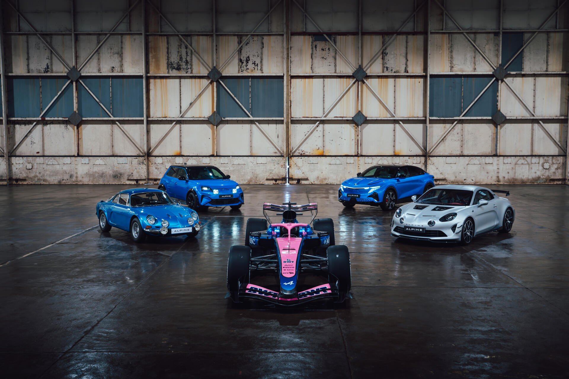Alpine A526 race car with sports cars in an industrial garage, featured in an 8K Ultra HD PC desktop wallpaper background.