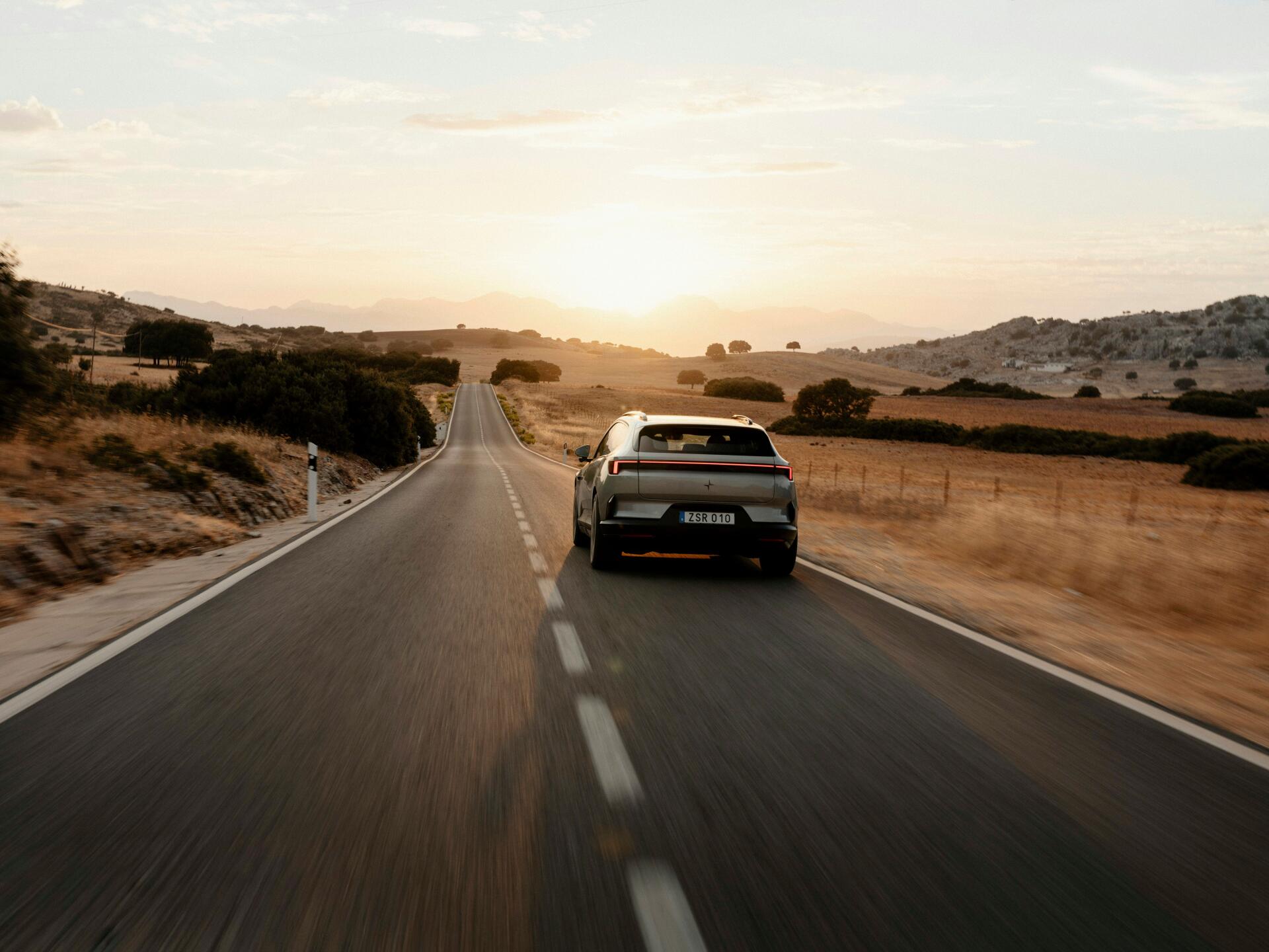 Polestar 4 SUV driving along a winding country road at sunset, featured in a 5K Ultra HD PC desktop wallpaper.
