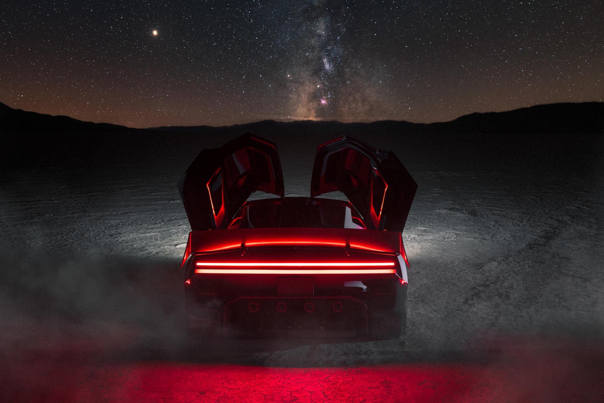 Tesla Roadster sports car with raised doors and glowing red taillights beneath a starry night sky, 2K Quad HD desktop wallpaper.