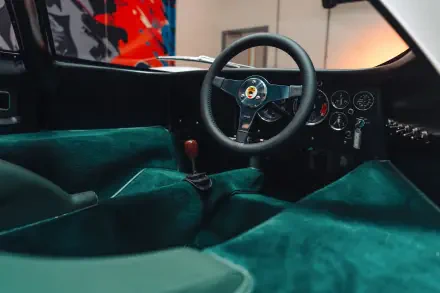 Vehicle interior of a McLaren G6GT: teal suede cockpit, classic steering wheel and manual shifter — 8K Ultra HD PC desktop wallpaper/background.