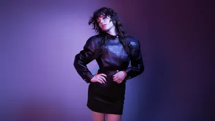 Young model in a black leather mini dress posing under purple studio lights; music-themed 5K Ultra HD PC desktop wallpaper.