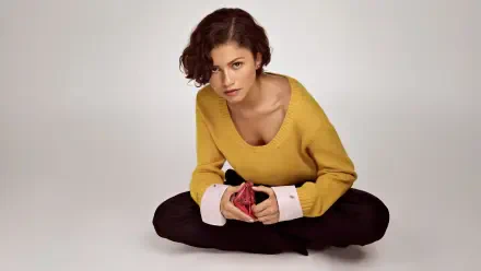 Young woman seated cross-legged on a neutral backdrop, wearing a mustard sweater and holding a red cloth — 5K Ultra HD PC desktop wallpaper/background.