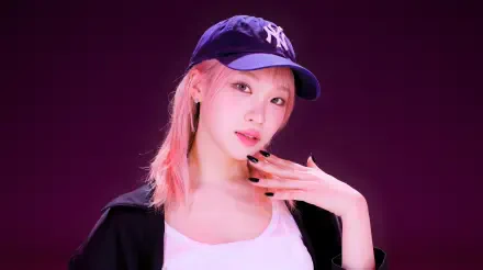 5K Ultra HD desktop wallpaper: portrait of a young woman in a navy baseball cap, pink-streaked hair, black jacket and white top posed against a deep purple background.
