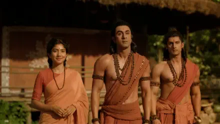 8K Ultra HD desktop wallpaper: three characters in saffron monk robes and prayer beads from Ramayana (2026), a woman and two men standing together in a rustic village setting.