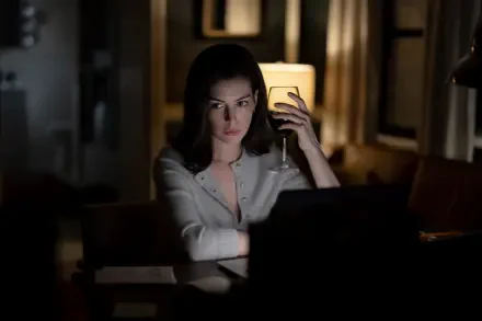 Anne Hathaway as Verity in a dimly lit room, holding a phone beside her laptop — 4K Ultra HD PC desktop wallpaper.