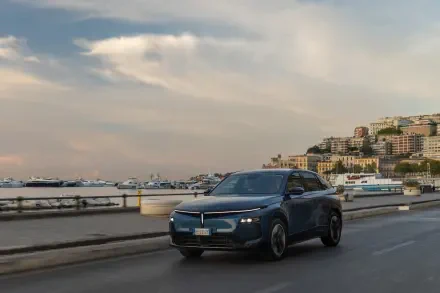 Lancia Gamma electric SUV driving along a coastal city road in an HD desktop wallpaper.