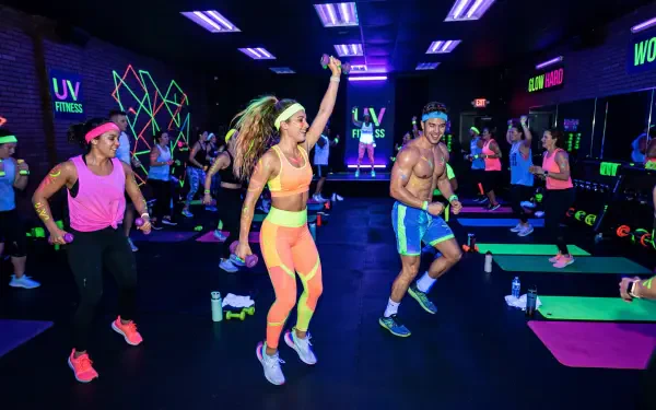 5K Ultra HD PC desktop wallpaper background: energetic group exercise class in a neon-lit gym, instructor leading aerobics with colorful activewear and glow accents.