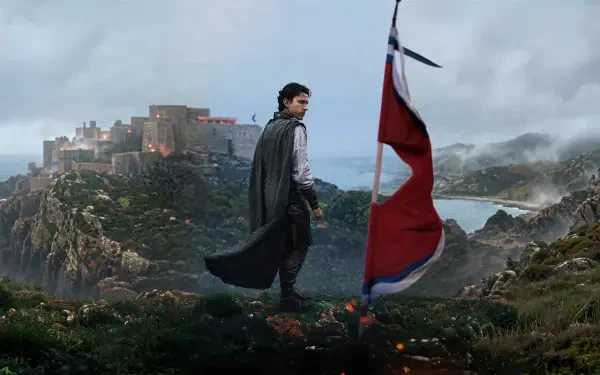 4K Ultra HD PC desktop wallpaper: cloaked hero on a windswept cliff by a tattered red banner, overlooking a coastal fortress and stormy sea — The Odyssey (2026).
