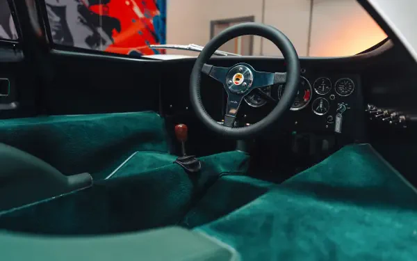 Vehicle interior of a McLaren G6GT: teal suede cockpit, classic steering wheel and manual shifter — 8K Ultra HD PC desktop wallpaper/background.