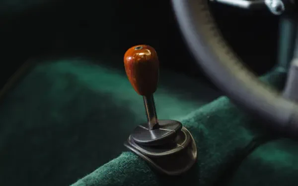 Close-up of a wooden gearshift knob and green interior upholstery in a McLaren G6GT, 8K Ultra HD PC desktop wallpaper.