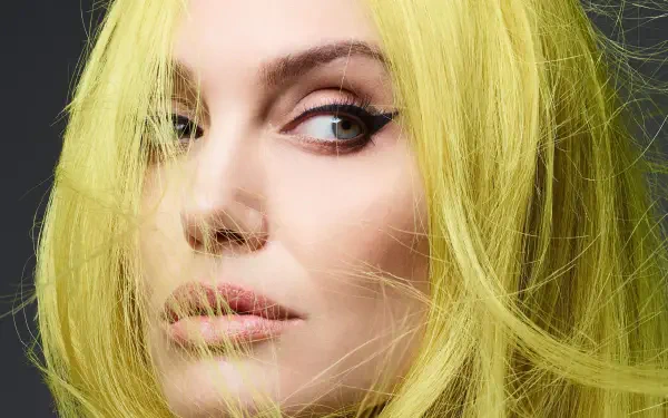 Close-up portrait of a woman with vivid yellow hair and winged eyeliner, soft skin tones, gazing off-frame — 4K Ultra HD PC desktop wallpaper/background.