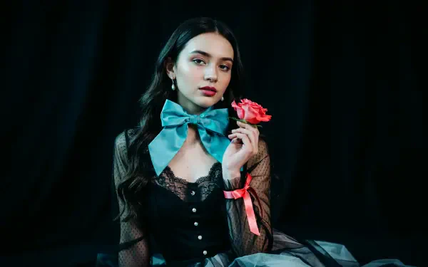 Dark coquette portrait of a woman in lace with a turquoise bow, holding a pink rose against a black backdrop — 4K Ultra HD PC desktop wallpaper background.