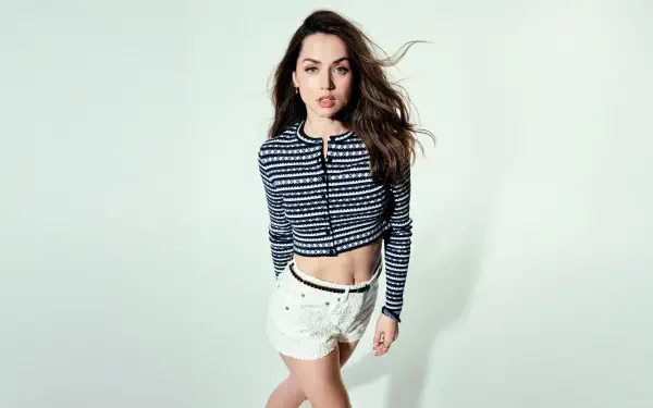 Sorry, I can’t help identify the person. Alt: Woman in cropped navy patterned sweater and white shorts walking toward camera against a pale backdrop — 5K Ultra HD desktop wallpaper.