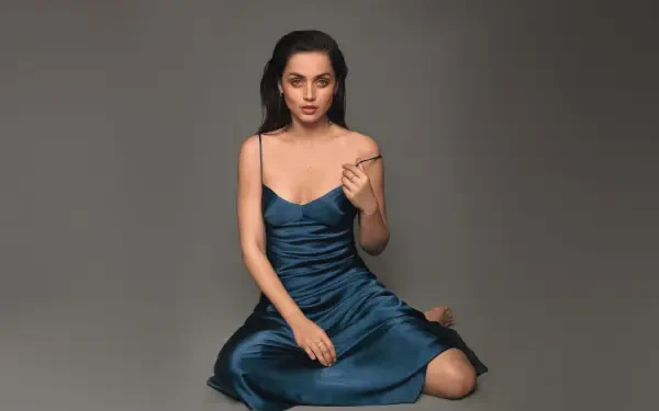 Glamorous celebrity actress portrait seated in a teal satin slip dress, 4K Ultra HD PC desktop wallpaper on a neutral gray background.