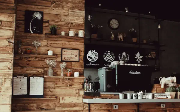Espresso Fall Cozy 5K Ultra HD PC desktop wallpaper: warm rustic coffee bar with espresso machine, wooden shelves, cups, plants and autumnal decor.
