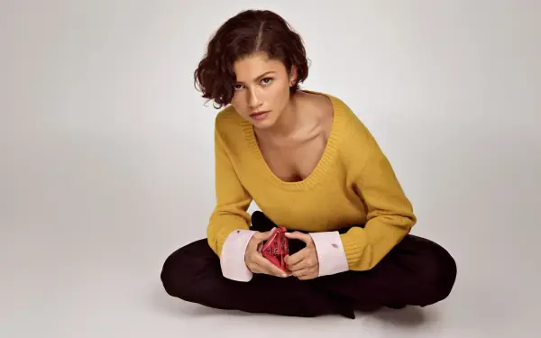 Young woman seated cross-legged on a neutral backdrop, wearing a mustard sweater and holding a red cloth — 5K Ultra HD PC desktop wallpaper/background.