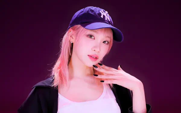 5K Ultra HD desktop wallpaper: portrait of a young woman in a navy baseball cap, pink-streaked hair, black jacket and white top posed against a deep purple background.