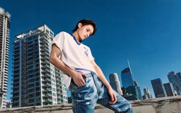Cortis — Color Outside the Lines 4K Ultra HD PC wallpaper: young man on a rooftop, leaning against a railing with a skyscraper cityscape under a clear blue sky.