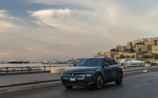 Lancia Gamma electric SUV driving along a coastal city road in an HD desktop wallpaper.