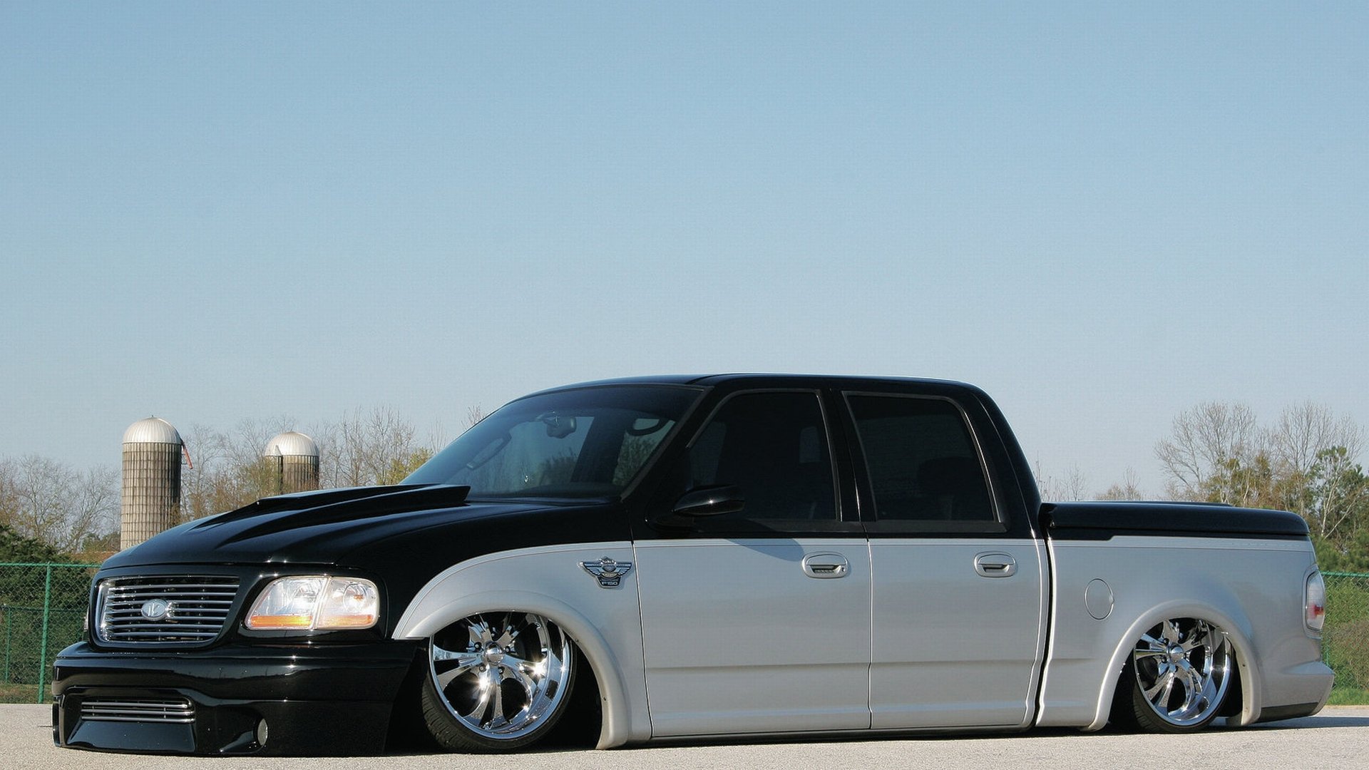 HD PC desktop wallpaper featuring a lowered Ford F-150 truck with a two-tone black and silver paint job against a clear sky backdrop.