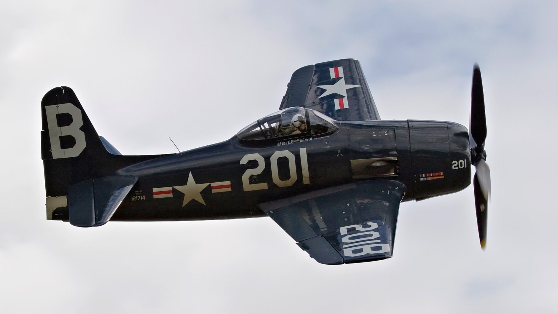 HD desktop wallpaper featuring a military Grumman F8F Bearcat aircraft in flight against a cloudy sky.