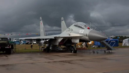 HD desktop wallpaper featuring a Sukhoi Su-30 military aircraft on a wet tarmac with a cloudy sky in the background.