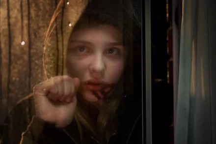 HD desktop wallpaper of Chloë Grace Moretz in the movie Let Me In, depicting her looking through a window with a solemn expression and a hand pressed against the glass.