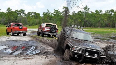HD PC desktop wallpaper: off-road vehicles on a muddy forest trail — a black SUV kicking up mud as two trucks behind tow and follow through deep puddles.